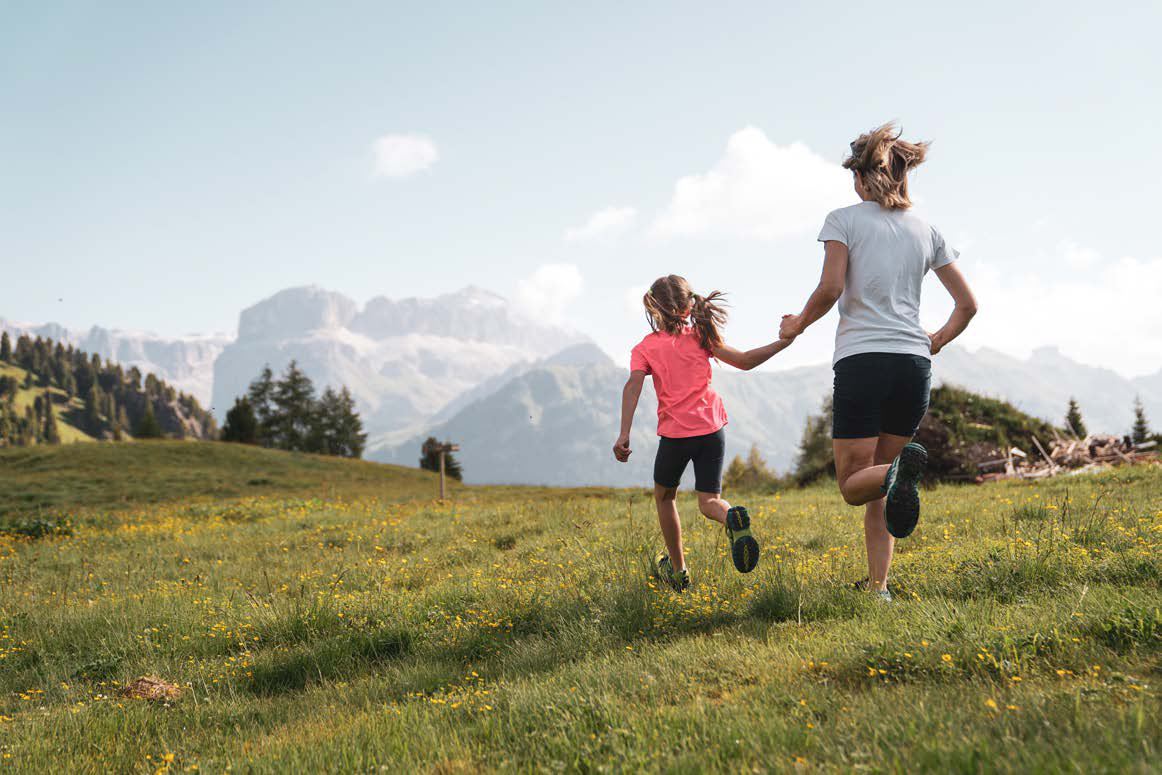 Mamma e bambina corrono in un prato davanti alle Dolomiti