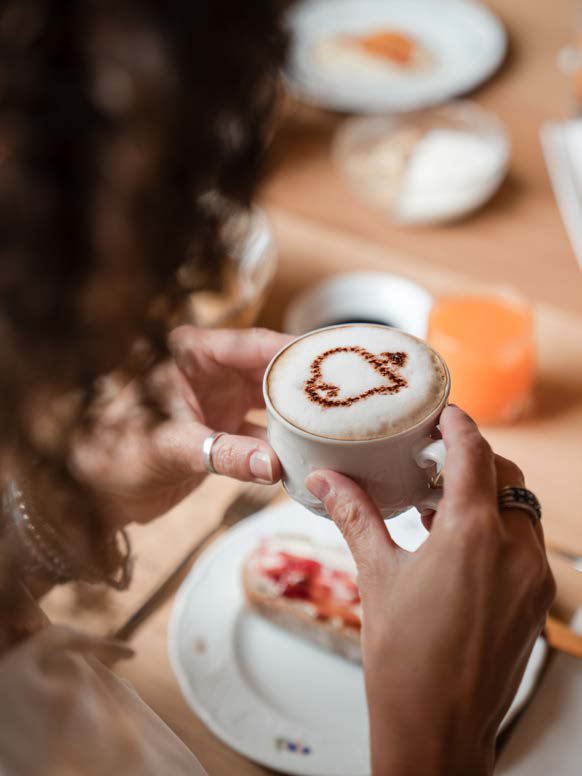 Mani reggono una tazza di cappuccino decorato durante la colazione