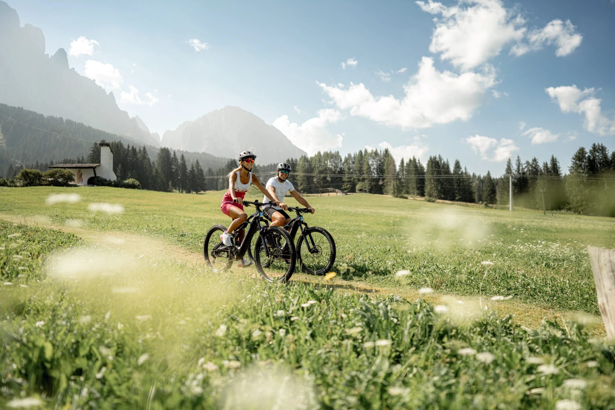 Due ciclisti pedalano in un prato fiorito di montagna