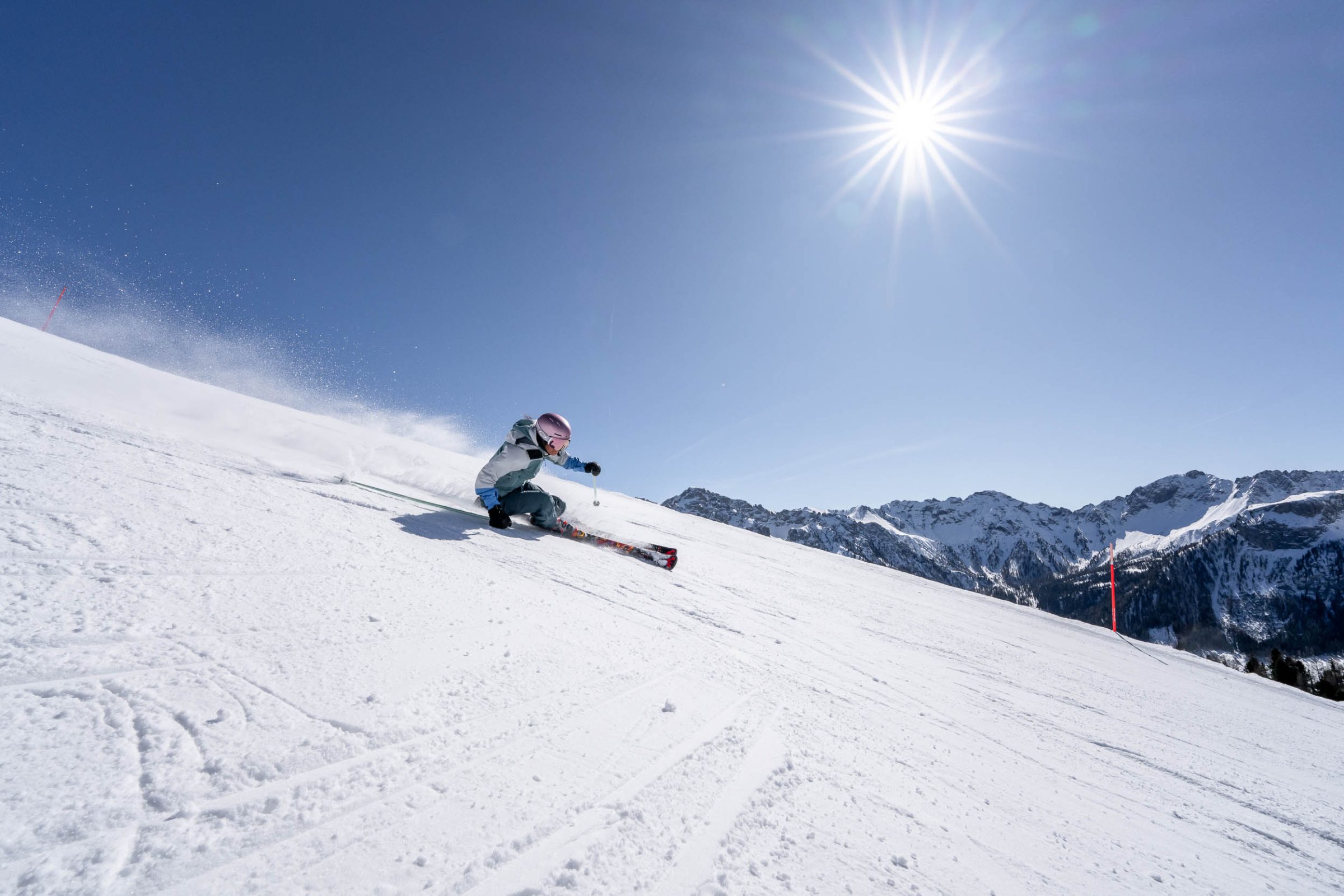 Sciatore in curva con il sole alto sopra le cime