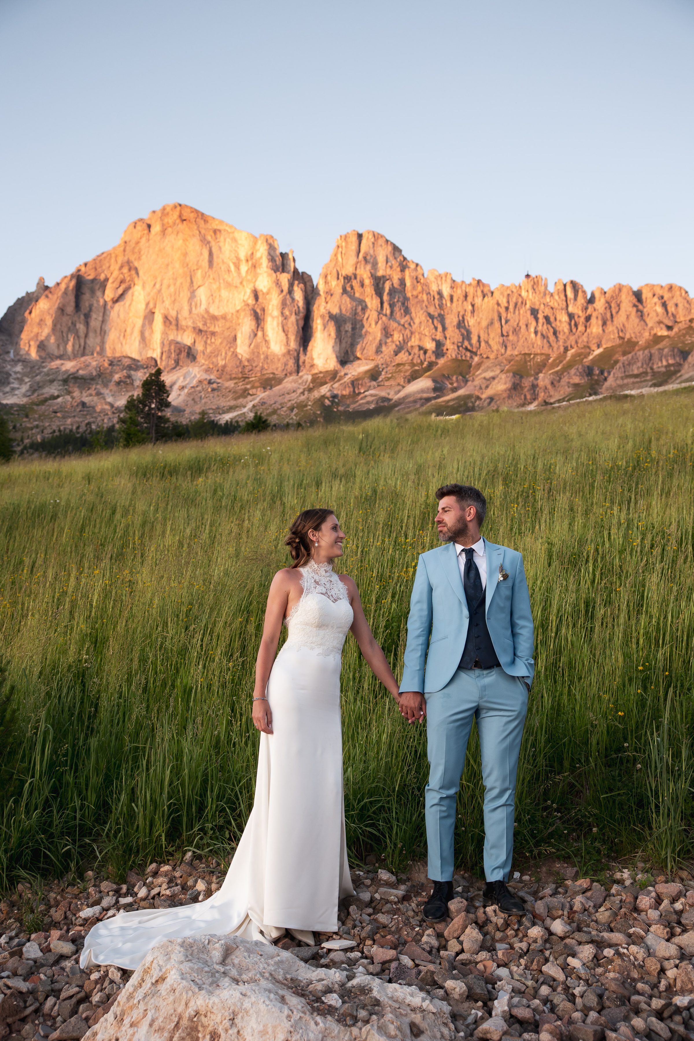 Sposi si tengono per mano in un prato con le Dolomiti sullo sfondo