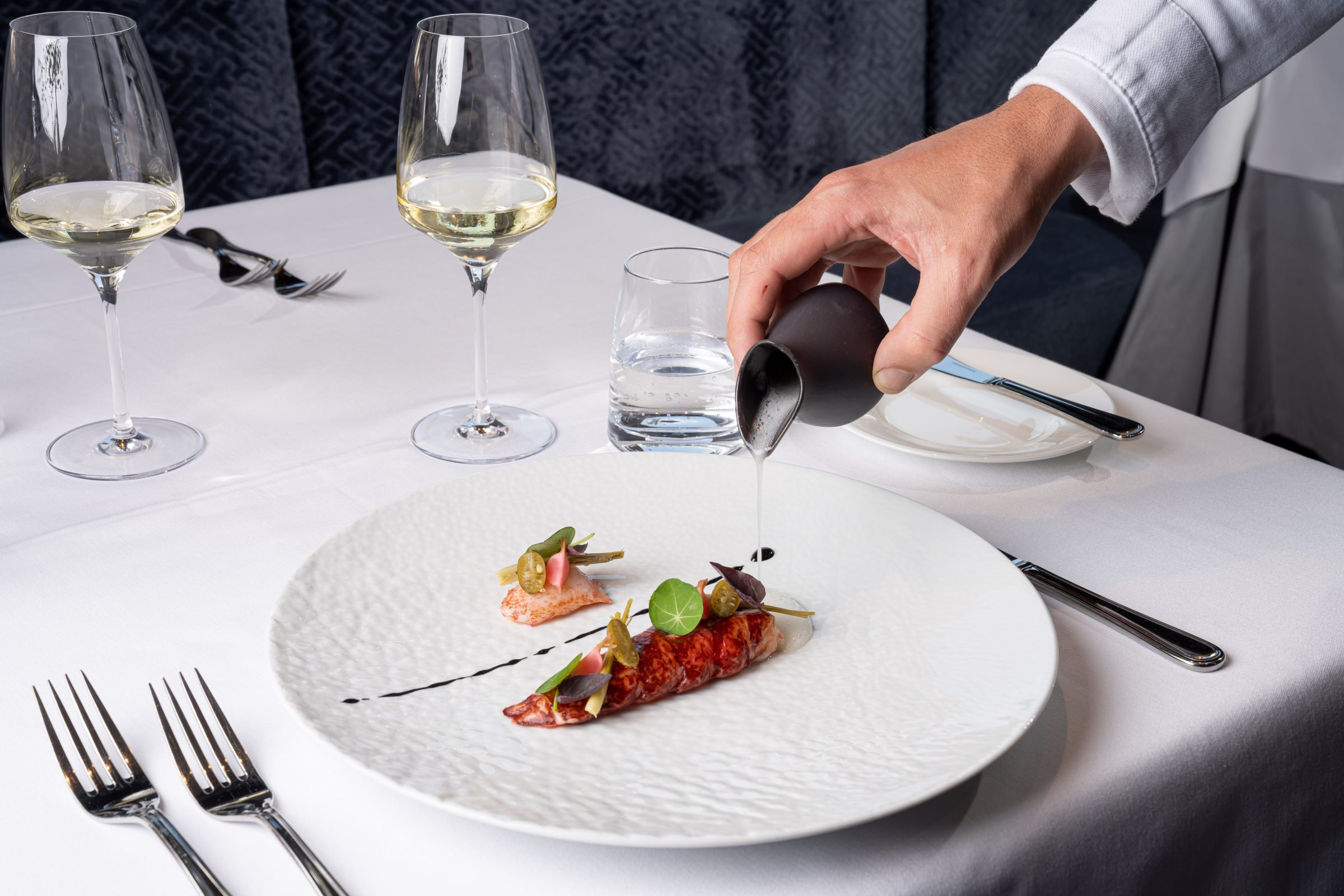 Piatto gourmet servito su tavola apparecchiata con calici di vino